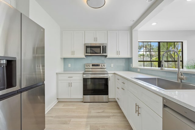 kitchen with sink, light hardwood / wood-style flooring, white cabinetry, stainless steel appliances, and tasteful backsplash