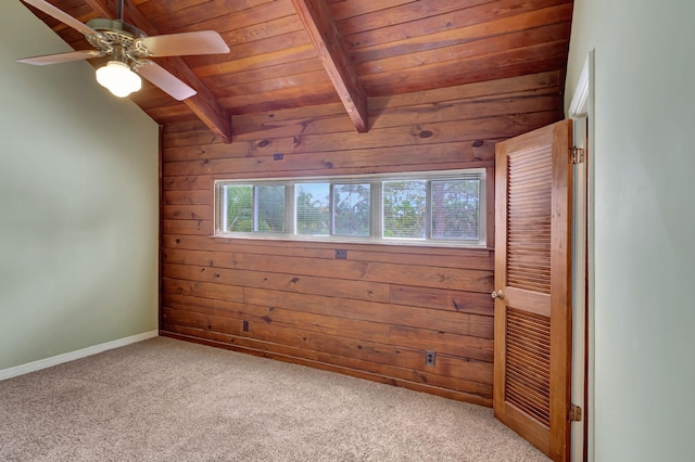 carpeted spare room with vaulted ceiling with beams, wood walls, wooden ceiling, and ceiling fan