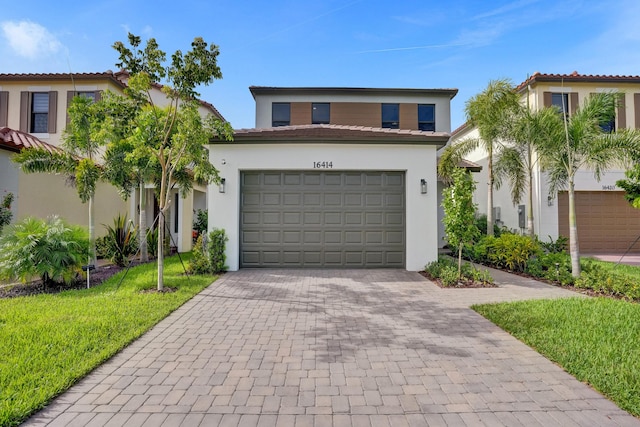 mediterranean / spanish home featuring a tile roof, decorative driveway, a front lawn, and stucco siding