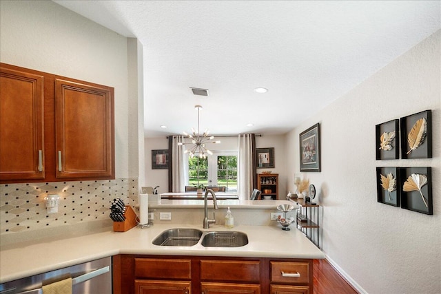 kitchen featuring pendant lighting, tasteful backsplash, a chandelier, kitchen peninsula, and sink