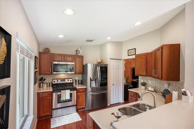 kitchen featuring vaulted ceiling, appliances with stainless steel finishes, dark wood-type flooring, kitchen peninsula, and sink