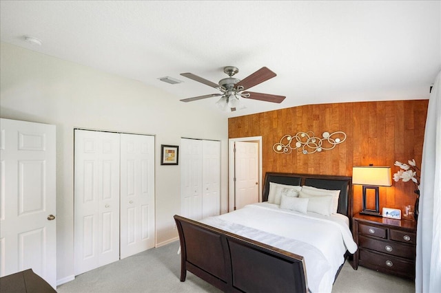 carpeted bedroom featuring lofted ceiling, ceiling fan, two closets, and wooden walls