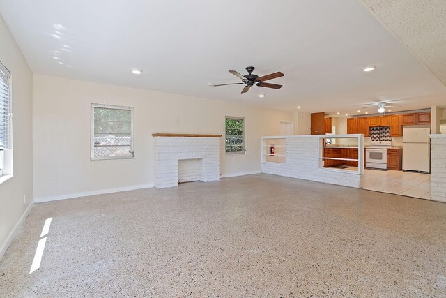 unfurnished living room featuring a wealth of natural light, ceiling fan, and a fireplace