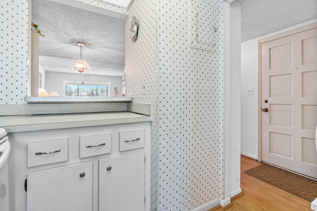 kitchen featuring a textured ceiling, light wood-style floors, light countertops, baseboards, and white cabinetry