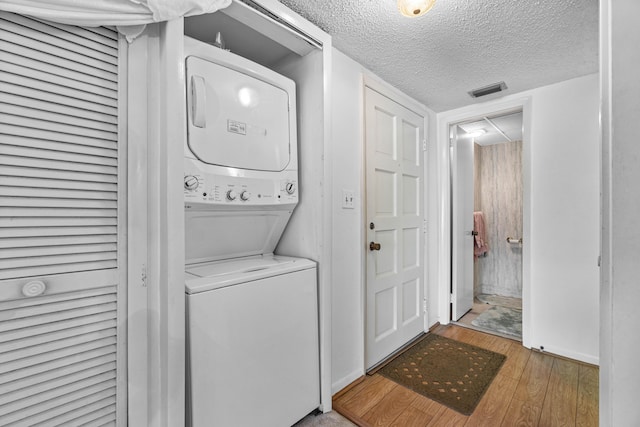 laundry area featuring stacked washer and clothes dryer, wood-type flooring, a textured ceiling, and baseboards