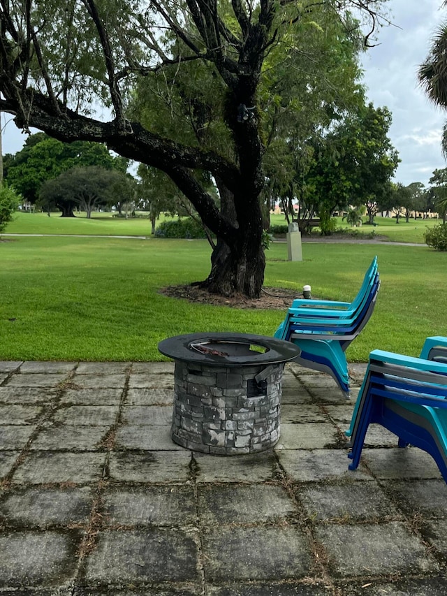 view of property's community featuring an outdoor fire pit, a patio area, and a lawn