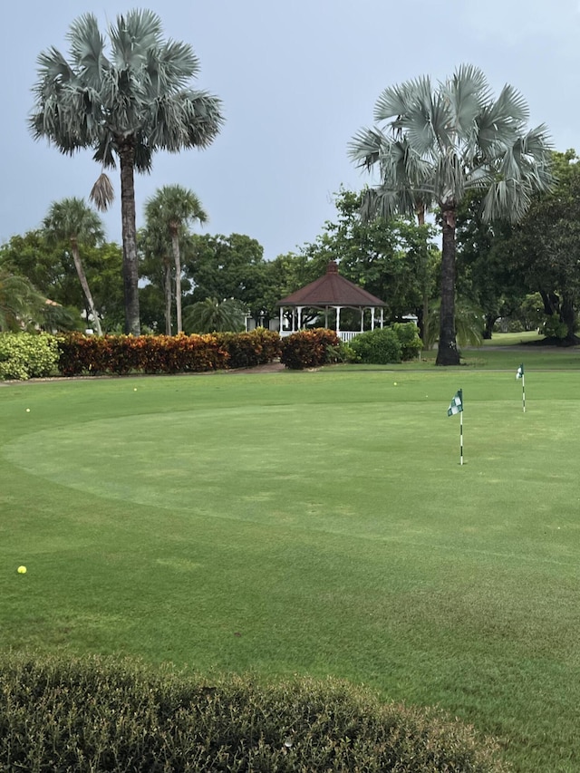 view of property's community with a gazebo, a putting area, a lawn, and view of golf course