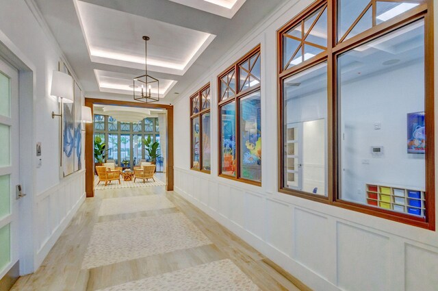 hallway featuring a raised ceiling, a notable chandelier, and light hardwood / wood-style floors