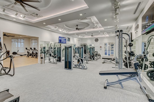 exercise room with ceiling fan, a raised ceiling, and light carpet