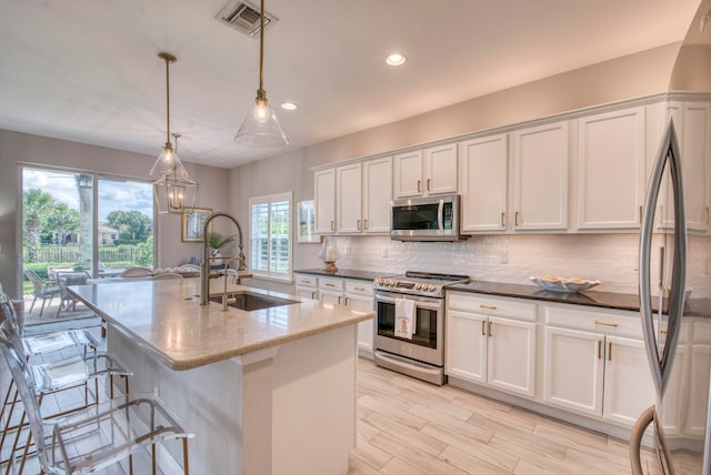 kitchen with stainless steel appliances, a kitchen island with sink, sink, decorative light fixtures, and white cabinets