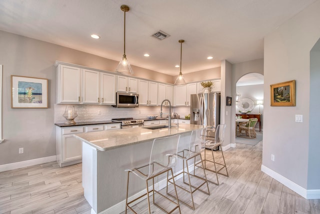 kitchen with a kitchen bar, light stone counters, stainless steel appliances, sink, and white cabinets