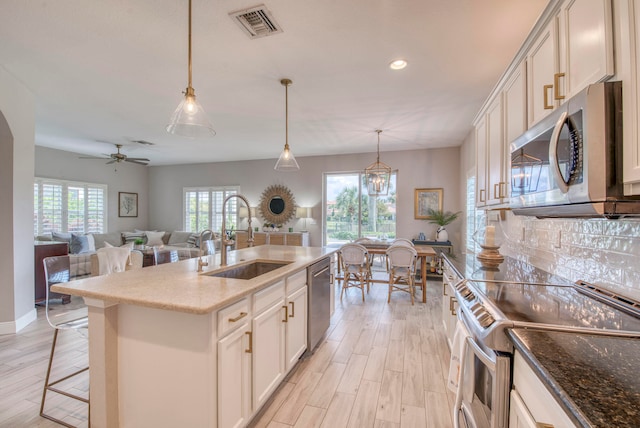 kitchen with sink, pendant lighting, a center island with sink, ceiling fan with notable chandelier, and appliances with stainless steel finishes