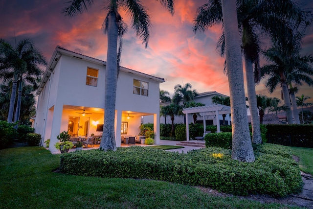 back house at dusk featuring a lawn, ceiling fan, a pergola, an outdoor living space, and a patio area