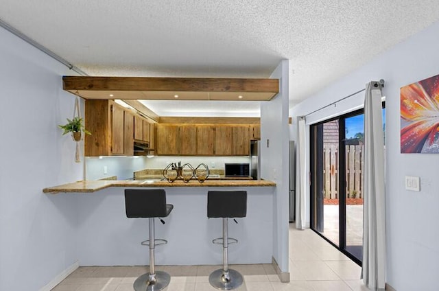 632 Springdale Cir, Palm Springs, FL 33461 - kitchen featuring brown cabinetry, a peninsula, a kitchen breakfast bar, baseboards, and a textured ceiling