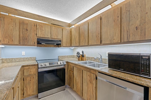 kitchen with a textured ceiling, sink, light stone countertops, appliances with stainless steel finishes, and light tile patterned flooring