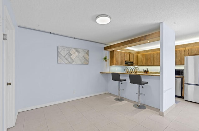 kitchen featuring appliances with stainless steel finishes, a textured ceiling, kitchen peninsula, and a kitchen breakfast bar