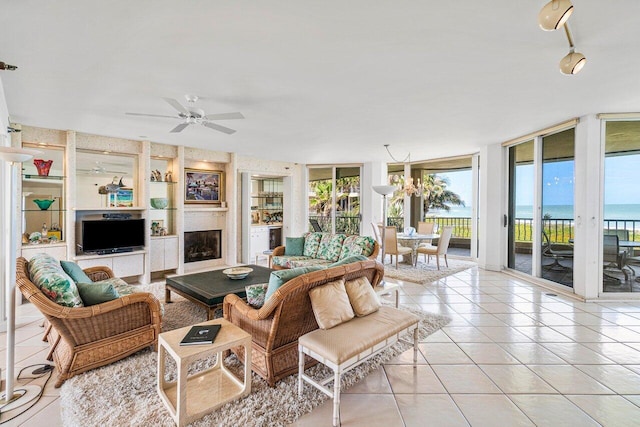 living room featuring ceiling fan, built in features, expansive windows, light tile patterned floors, and a fireplace