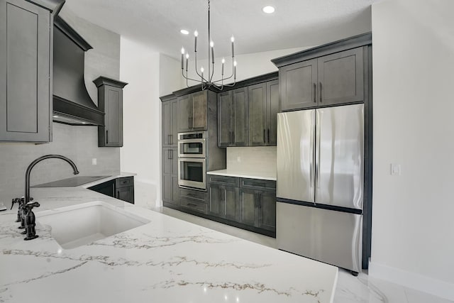 kitchen with appliances with stainless steel finishes, light stone counters, a chandelier, sink, and pendant lighting