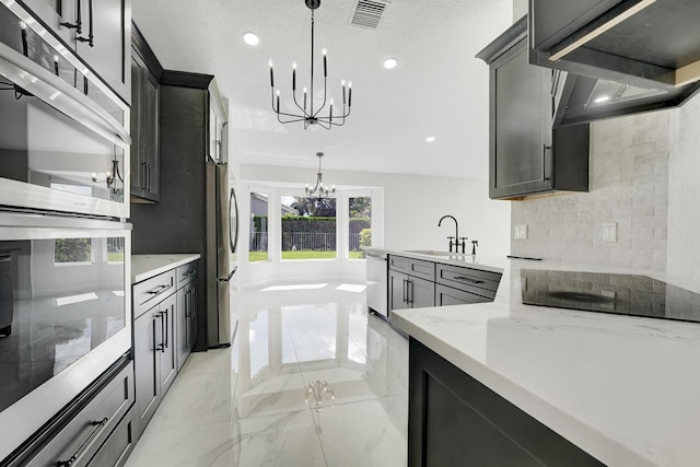 kitchen with a chandelier, stainless steel appliances, sink, light stone countertops, and hanging light fixtures