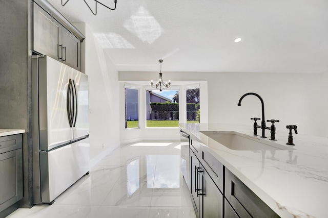 kitchen featuring pendant lighting, appliances with stainless steel finishes, sink, a chandelier, and light stone counters