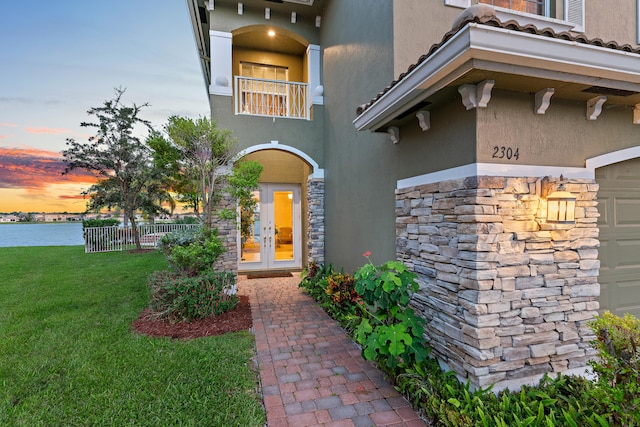 exterior entry at dusk with a lawn, a balcony, and french doors