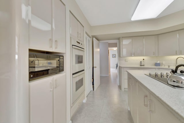 kitchen with white cabinets, tasteful backsplash, white double oven, light tile patterned flooring, and stovetop