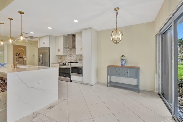 kitchen featuring wall chimney range hood, hanging light fixtures, appliances with stainless steel finishes, white cabinetry, and sink