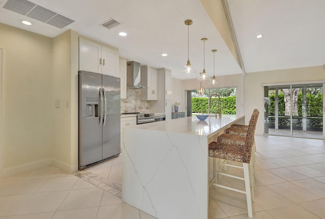 kitchen featuring backsplash, hanging light fixtures, white cabinetry, stainless steel appliances, and wall chimney exhaust hood