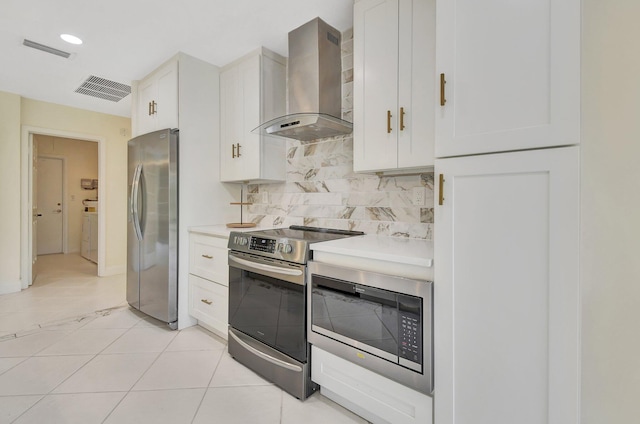 kitchen featuring wall chimney range hood, stainless steel appliances, light tile patterned floors, white cabinets, and tasteful backsplash