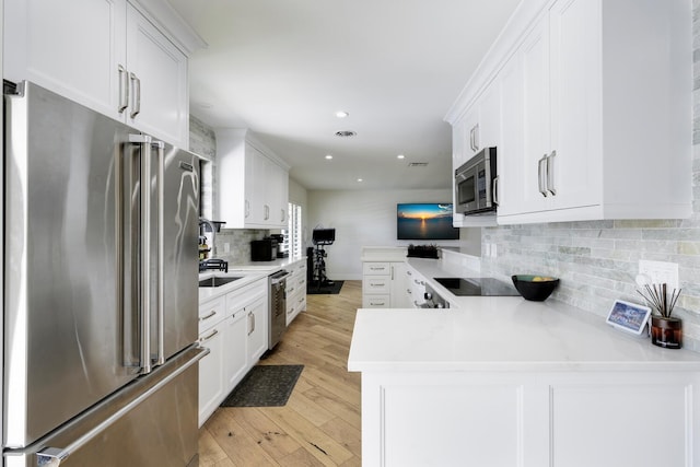 kitchen with light hardwood / wood-style floors, kitchen peninsula, white cabinetry, and appliances with stainless steel finishes