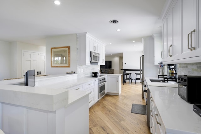 kitchen featuring white cabinets, decorative backsplash, light hardwood / wood-style floors, and stainless steel appliances