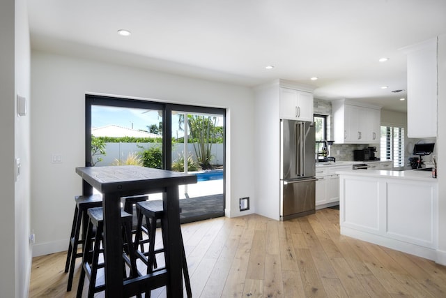 kitchen featuring decorative backsplash, high end refrigerator, light hardwood / wood-style flooring, and white cabinetry