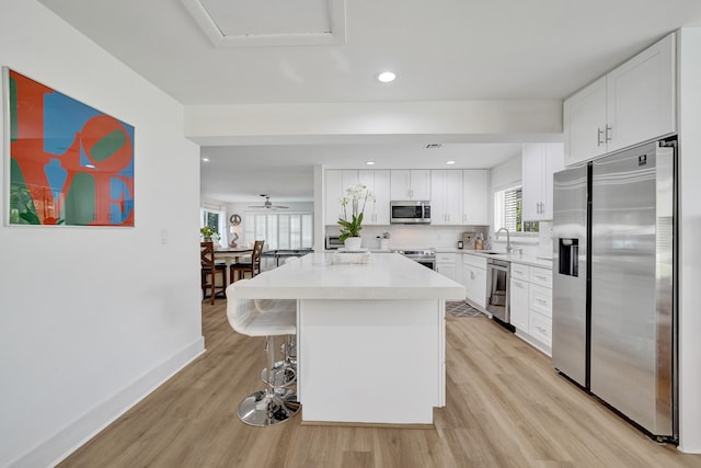 kitchen with a kitchen bar, stainless steel appliances, a kitchen island, light hardwood / wood-style floors, and white cabinetry