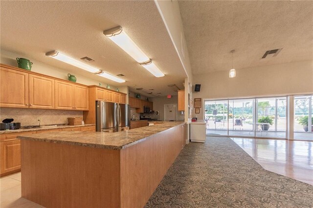 kitchen with stainless steel fridge, a textured ceiling, kitchen peninsula, light stone countertops, and decorative backsplash