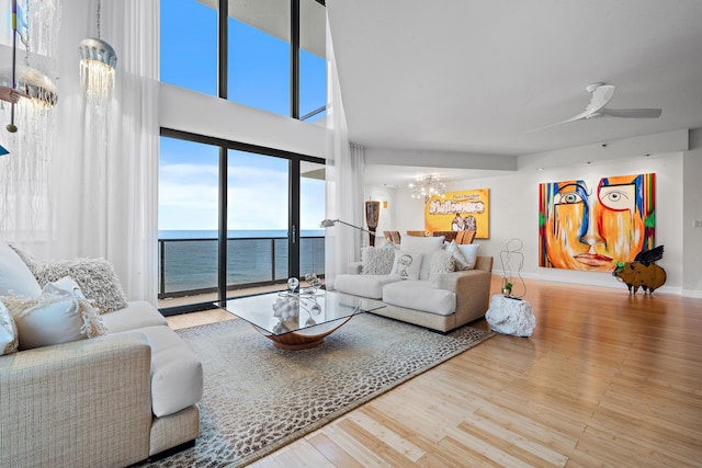 living room featuring ceiling fan with notable chandelier, a water view, and wood-type flooring