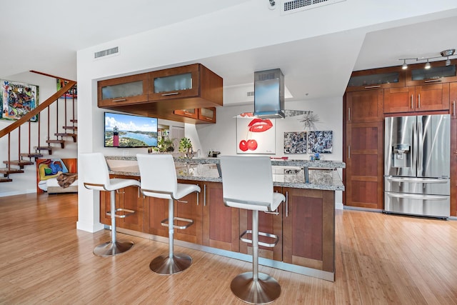 kitchen with light hardwood / wood-style floors, a breakfast bar, light stone countertops, stainless steel fridge, and island range hood