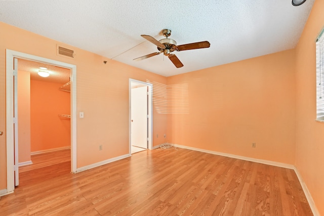 unfurnished bedroom with a spacious closet, ceiling fan, a textured ceiling, a closet, and light wood-type flooring