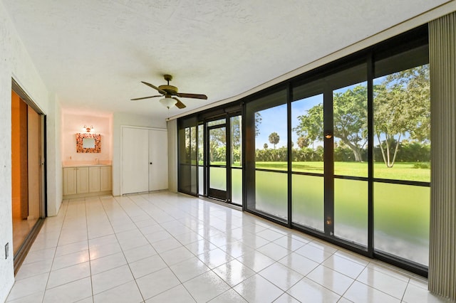 tiled empty room with a textured ceiling, expansive windows, and ceiling fan