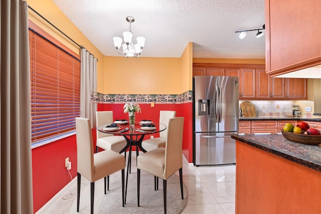 dining area featuring light tile patterned flooring, track lighting, a textured ceiling, and a notable chandelier