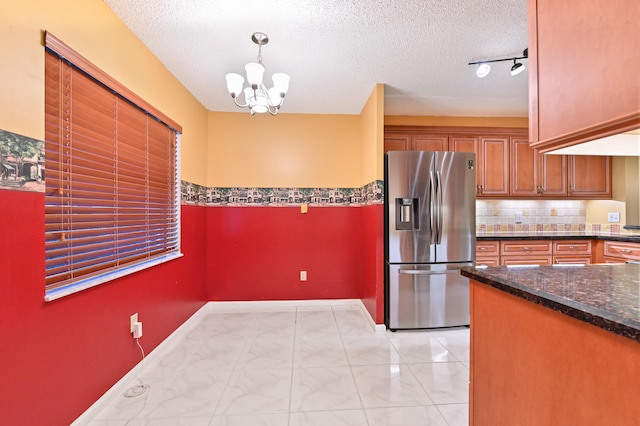 kitchen featuring stainless steel refrigerator with ice dispenser, a textured ceiling, hanging light fixtures, and dark stone counters