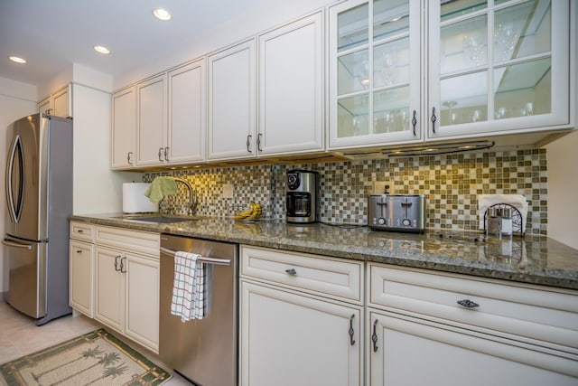 kitchen with dark stone countertops, backsplash, sink, appliances with stainless steel finishes, and white cabinets