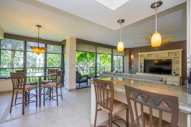 kitchen featuring decorative light fixtures, ceiling fan, light stone counters, and a breakfast bar