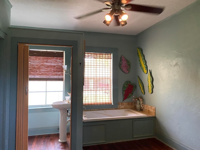 bathroom featuring ceiling fan, wood-type flooring, a tub to relax in, and a wealth of natural light