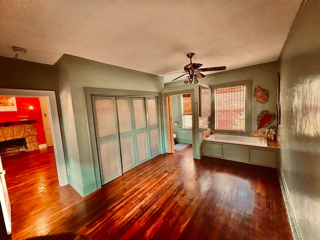 unfurnished bedroom featuring hardwood / wood-style floors, a textured ceiling, a stone fireplace, and ceiling fan