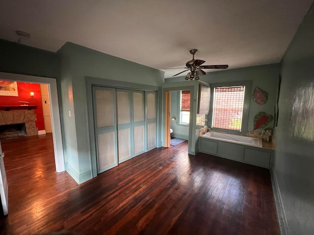 unfurnished bedroom with a stone fireplace, ceiling fan, and dark hardwood / wood-style floors