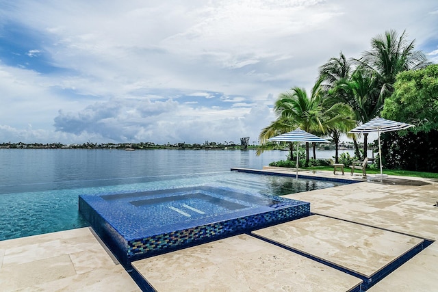 view of pool featuring an in ground hot tub, a water view, and a patio area