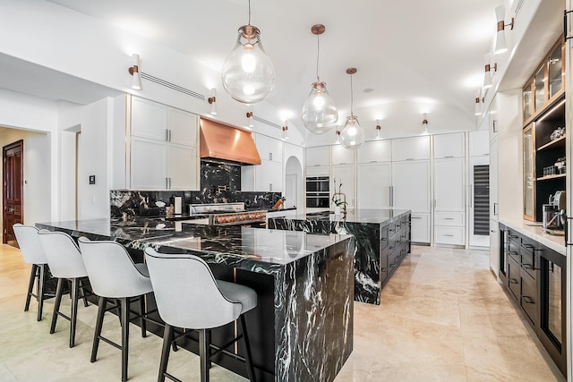 kitchen featuring extractor fan, decorative light fixtures, dark stone countertops, a large island with sink, and white cabinets