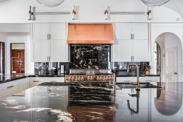 kitchen featuring white cabinets, backsplash, dark stone counters, range, and custom range hood