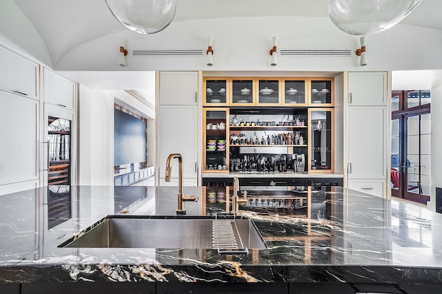 interior space with dark stone countertops, sink, lofted ceiling, and white cabinets