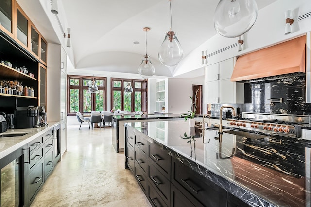 kitchen featuring premium range hood, decorative light fixtures, lofted ceiling, decorative backsplash, and light stone countertops